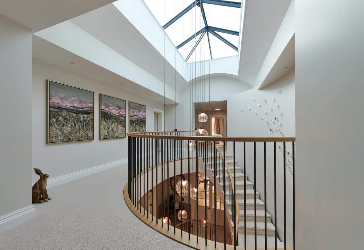 Curved staircase with black metal spindles and an oak handrail beneath a large skylight, with pendant lights suspended through the stairwell.